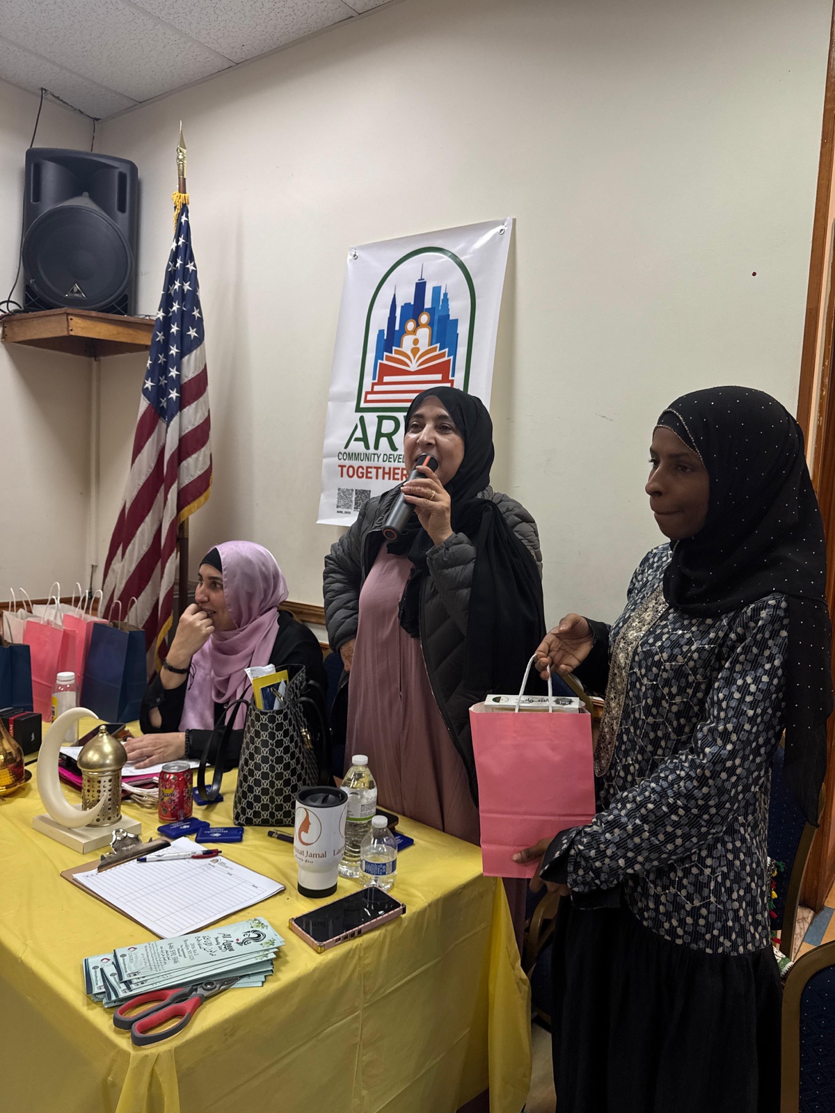 Speaker addressing families at an ARWA community gathering with gift bags and the ARWA banner